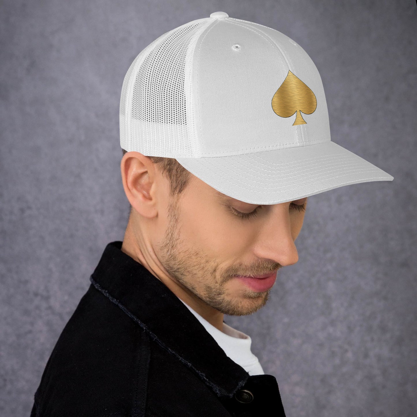 Mann mit weißen Trucker-Cap, goldenes Pik-Symbol auf der Vorderseite, Kopf leicht nach unten geneigt.